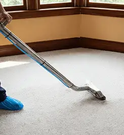 Steam carpet cleaning technician using a hot-water extraction wand on a residential carpet, wearing blue protective shoe covers Detroit, MI.