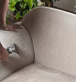 Professional upholstery cleaner deep-cleaning a fabric sofa with a handheld extraction tool and hose Detroit, MI.